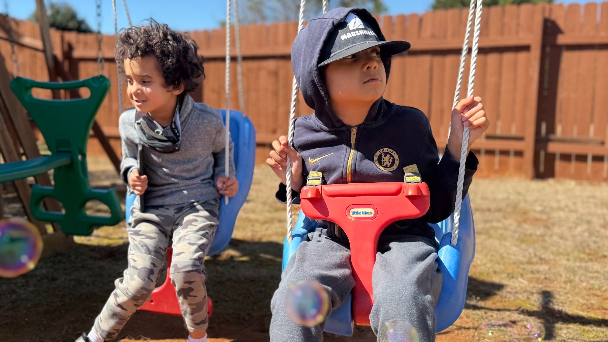Twin brothers on swings — one in a regular swing, one in an adaptive swing with safety support